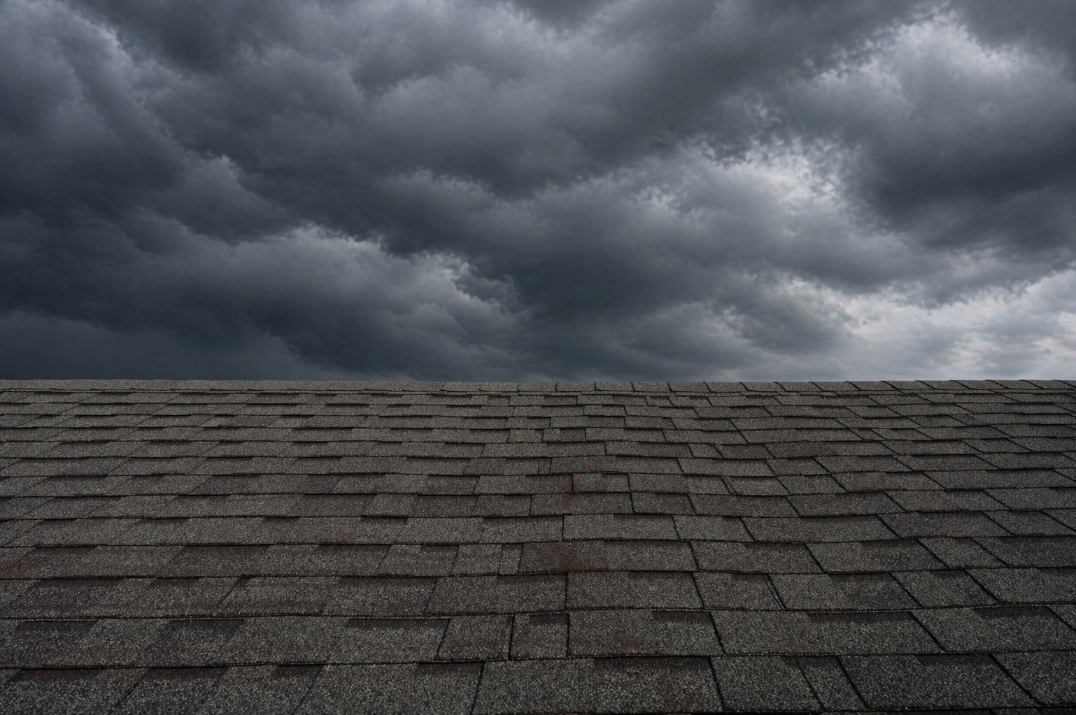 Asphalt shingle roof under dark storm clouds highlighting need for roof inspection